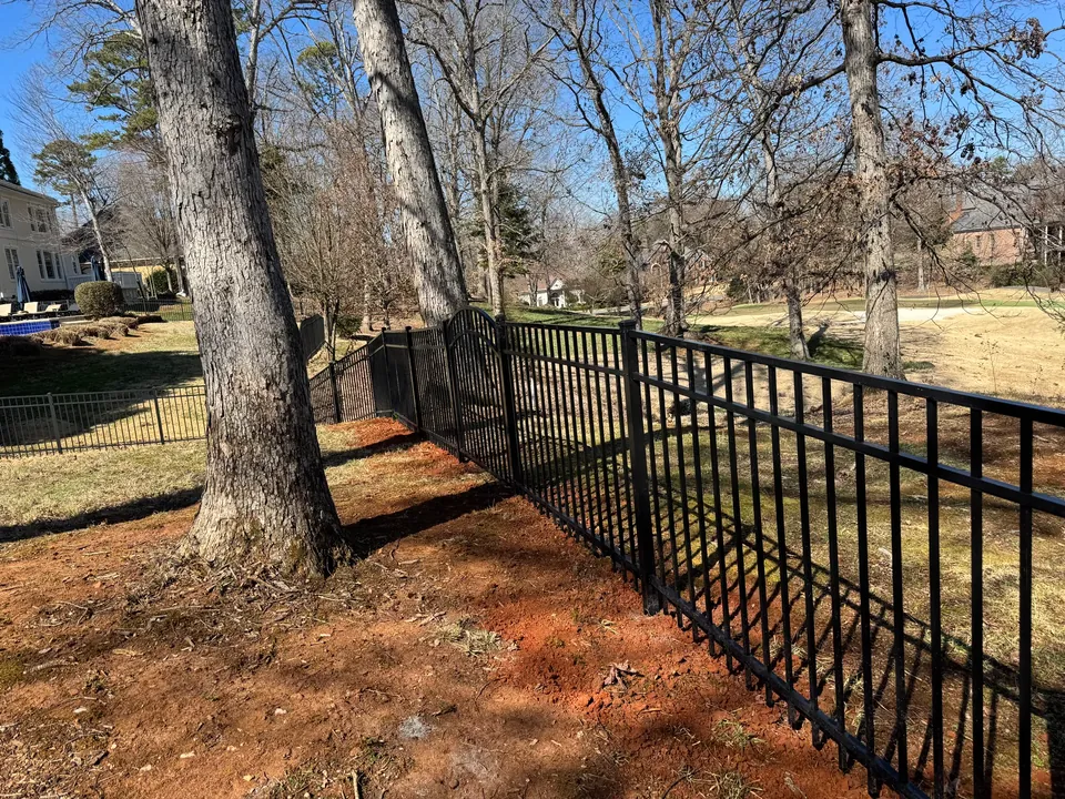 Black aluminum fence on a sloped yard among large trees.