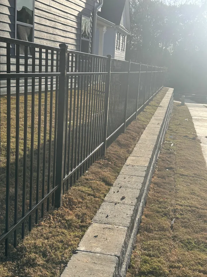 Black aluminum fence on a block retaining wall in morning sun.