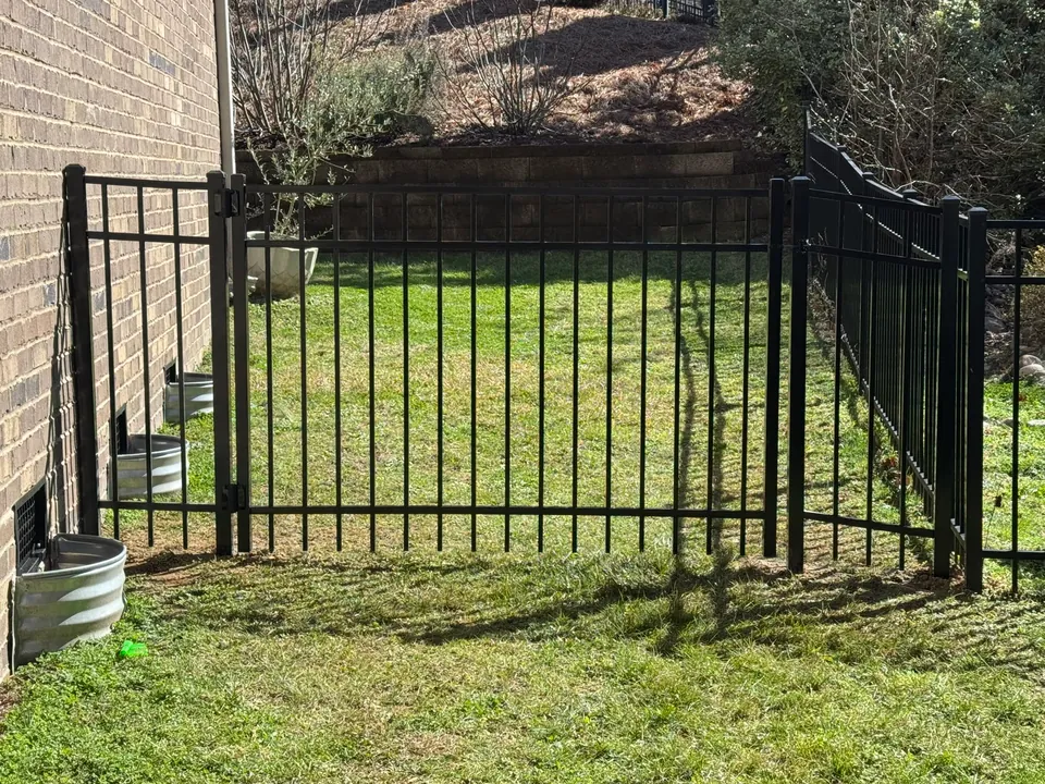 Black aluminum fence and walk gate enclosing a side yard against a brick house.