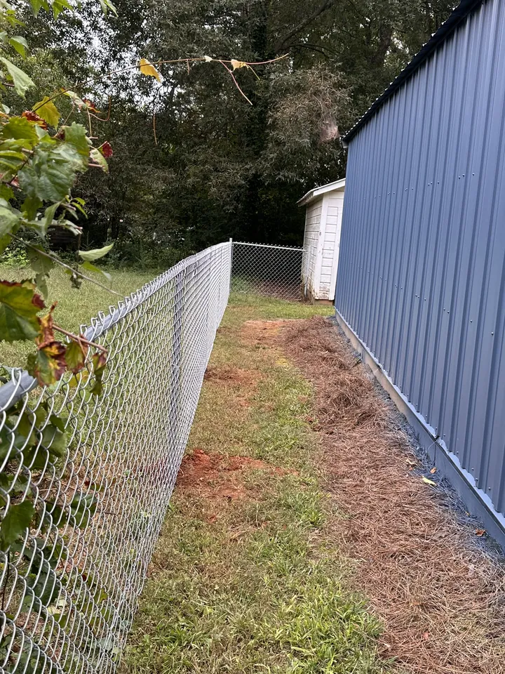 Galvanized chain link fence running between a lawn strip and a metal building.