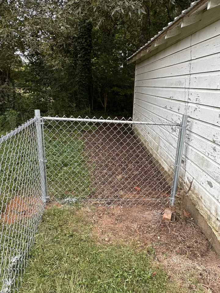 Galvanized chain link fence and gate beside a white outbuilding.