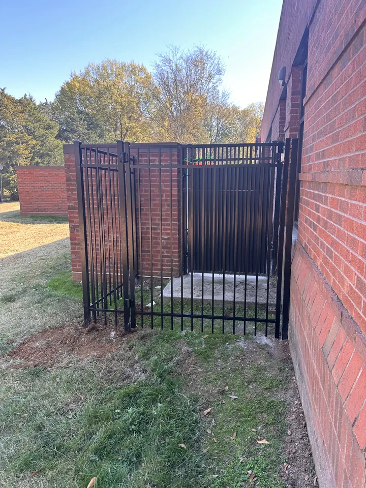 Black aluminum enclosure and gate against a brick commercial building.