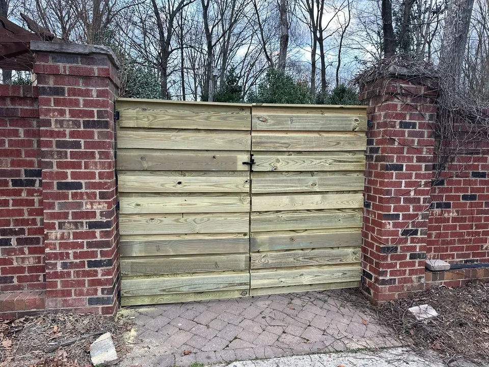 Horizontal wood slat gate between brick pillars over a paver walk.
