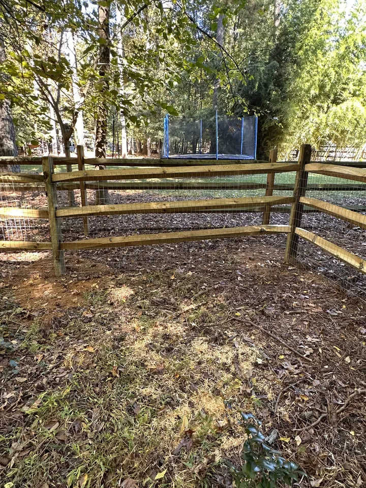 Wood split rail fence corner around a wooded backyard.