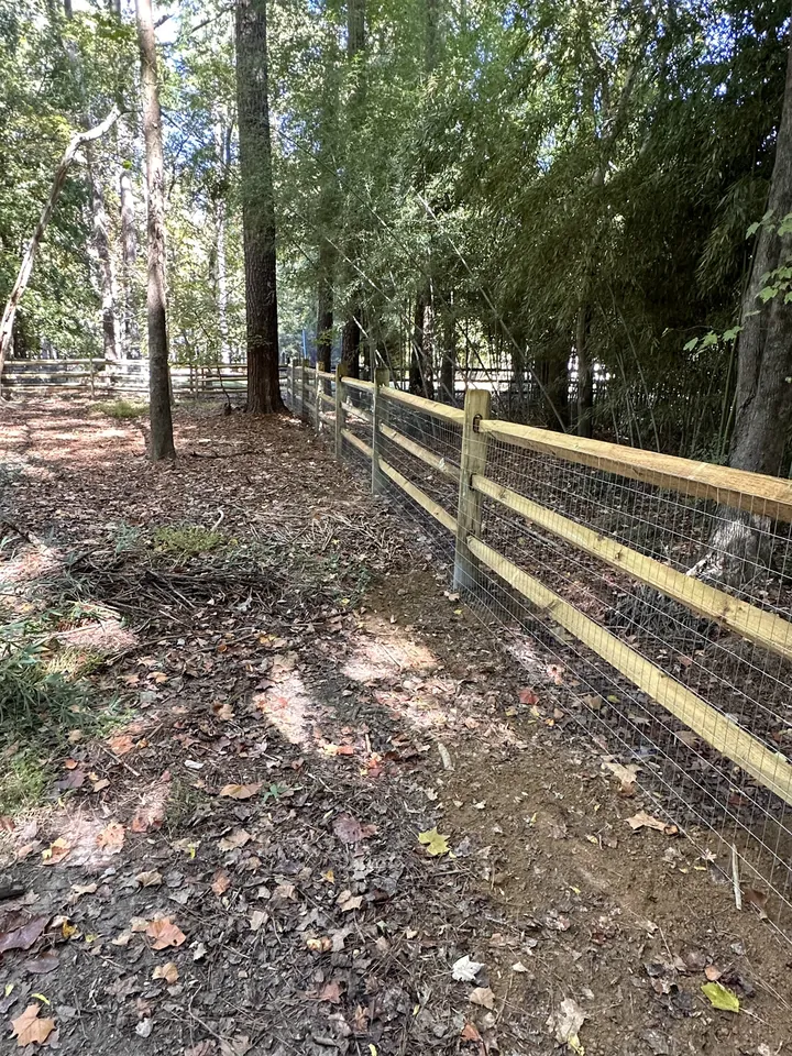 Wood split rail fence with wire mesh along a wooded slope.