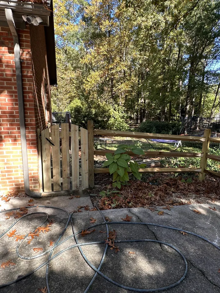 Wood split rail fence and picket gate beside a brick house.