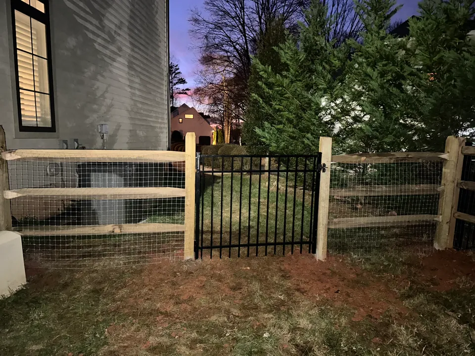 Wood split rail fence with wire mesh and a black aluminum walk gate.