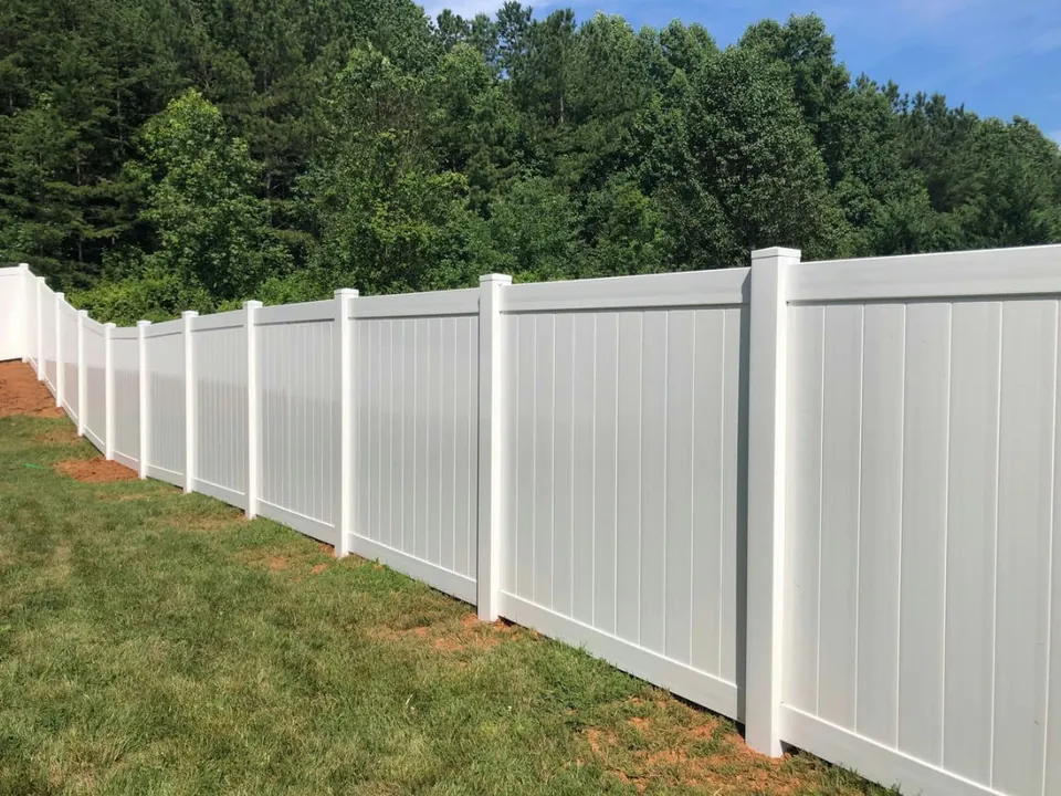 White vinyl privacy fence running along a backyard tree line.