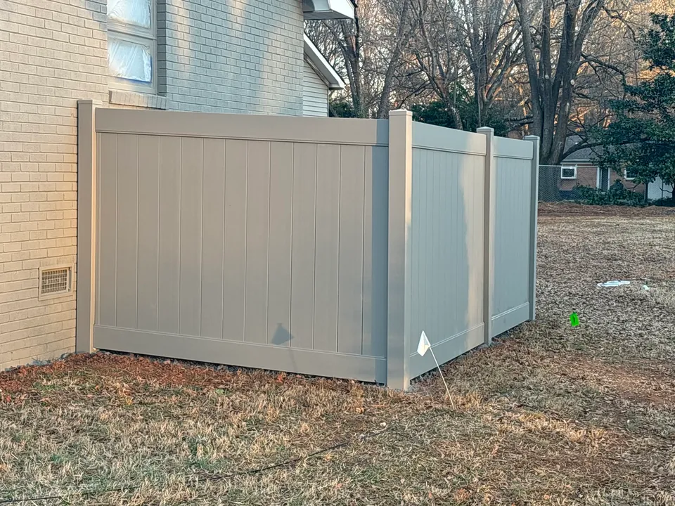 Tan vinyl privacy fence enclosure beside a house.