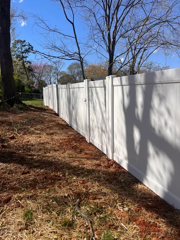 White vinyl privacy fence along a pine straw bed.