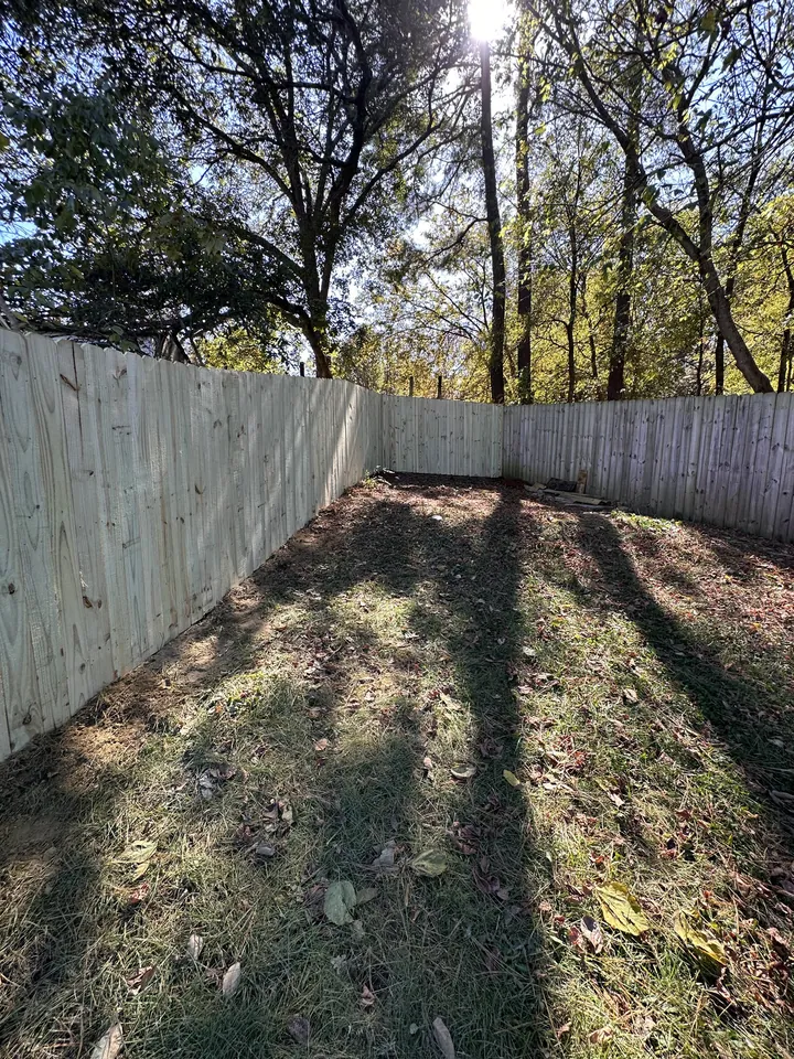 Pressure treated wood privacy fence corner on a sloped wooded lot.